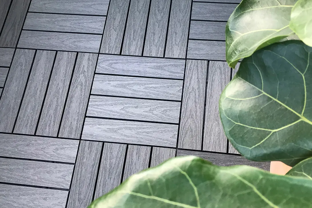 Woodlon terrasseheller i trekompositt med trestruktur lagt i rutemønster ved grønn plante