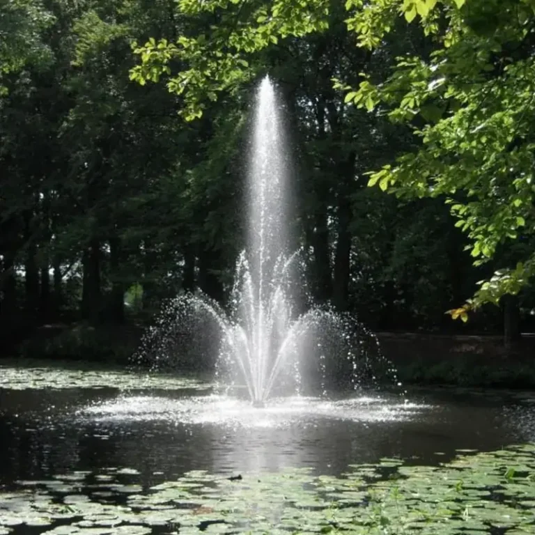 Vulkandyse sender en høy, sprudlende vannsøyle opp midt i en dam med vannliljeblader