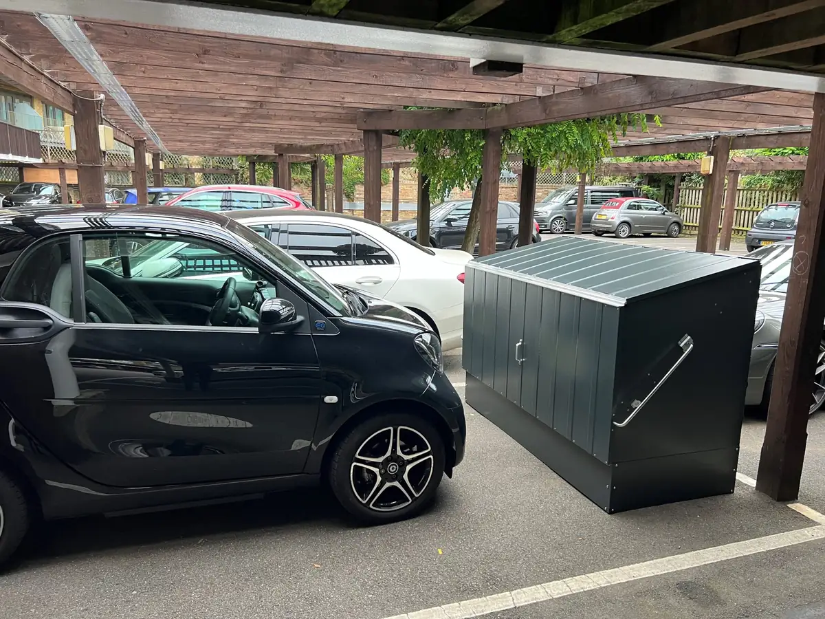 Lukket gop Bicycle Store sykkelgarasje i antrasitt ved siden av en bil under carporten