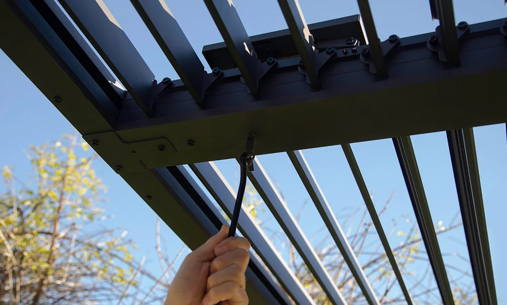 Hånd som vrir sveiven under taket på gop Novara pergola for å åpne lamellene