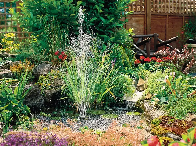 Hozelock EasyClear 6000 lager en høy fontene i en hagedam omgitt av sivplanter, stein og blomster
