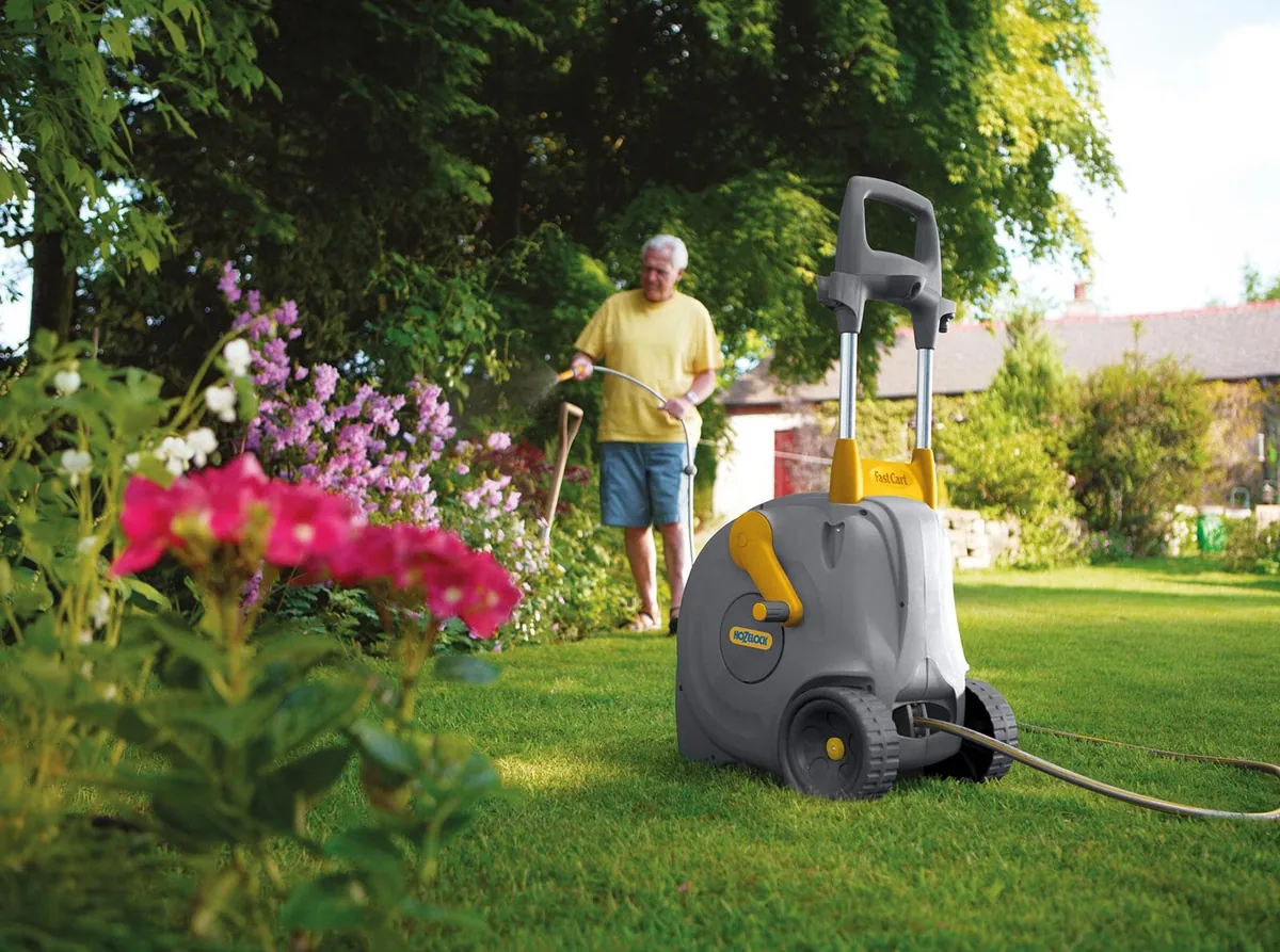 Hozelock Fast Cart slangevogn med 40 m slange på plenen mens blomsterbedet vannes
