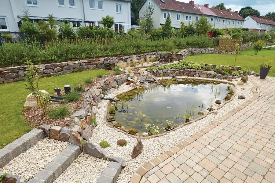 Etter: ferdig hagedam med steinkant, vannplanter og grus ved den steinbelagte terrassen