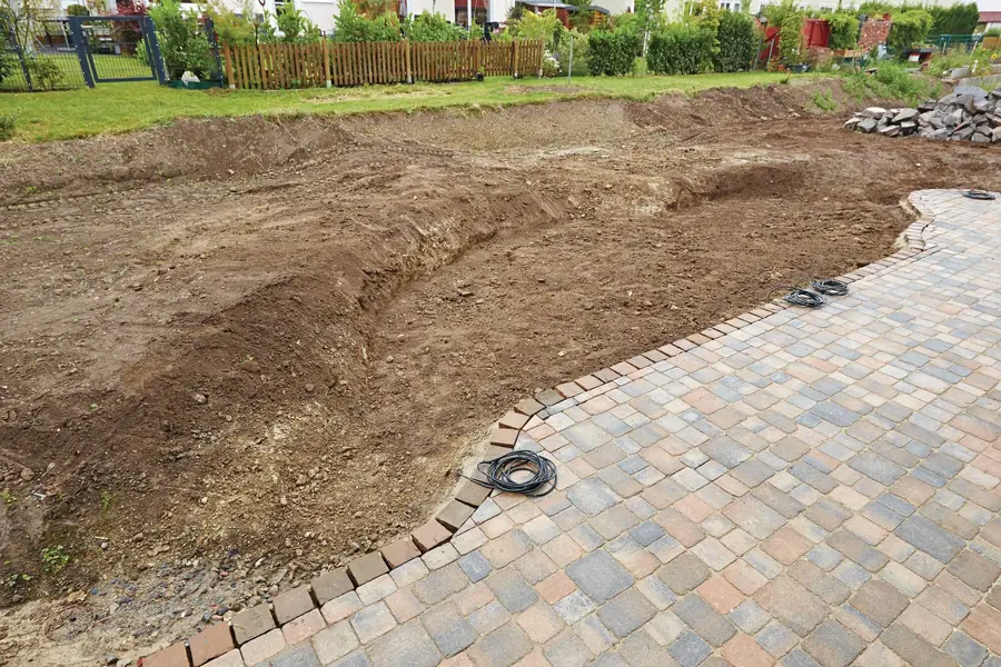 Før: utgravd tomt der hagedammen skal ligge, ved en nylagt steinbelagt terrasse