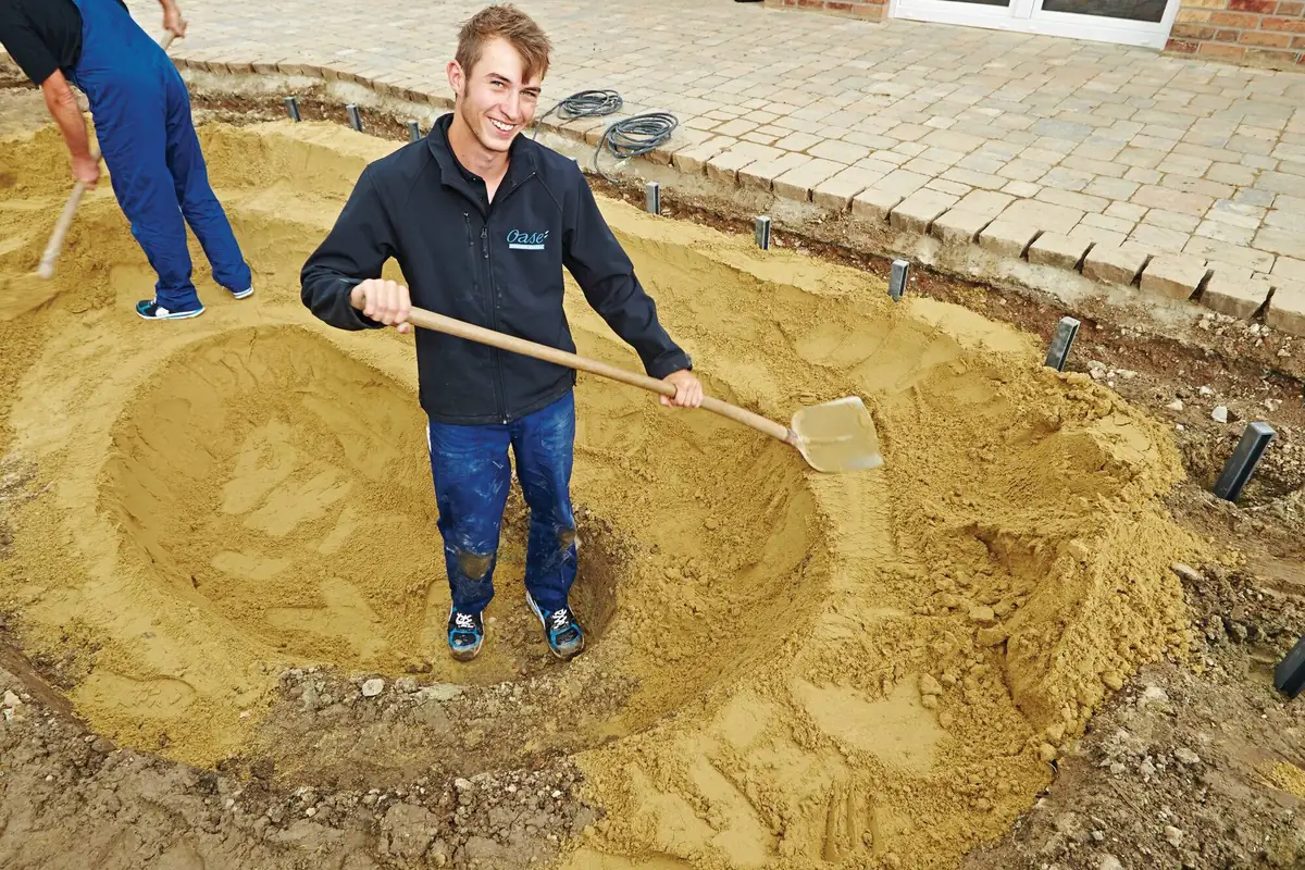 Sand jevnes ut med spade i bunnen av en utgravd hagedam