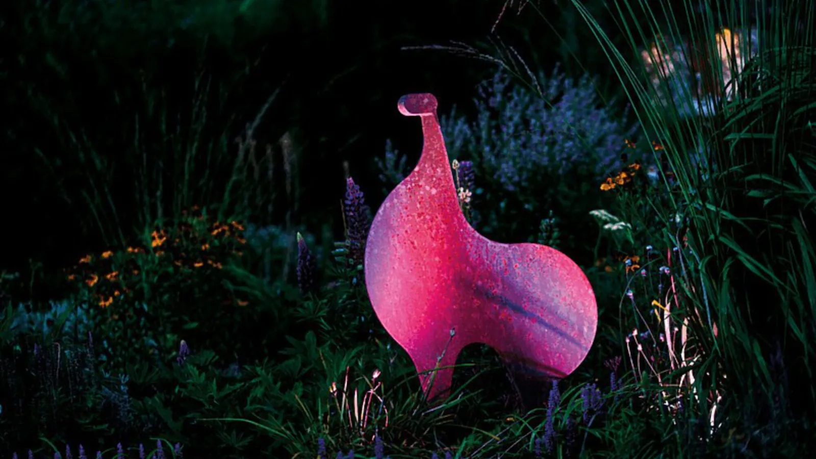 Hageskulptur badet i rosa fargelys fra en LunAqua Connect RGB-spot blant gress og busker om kvelden