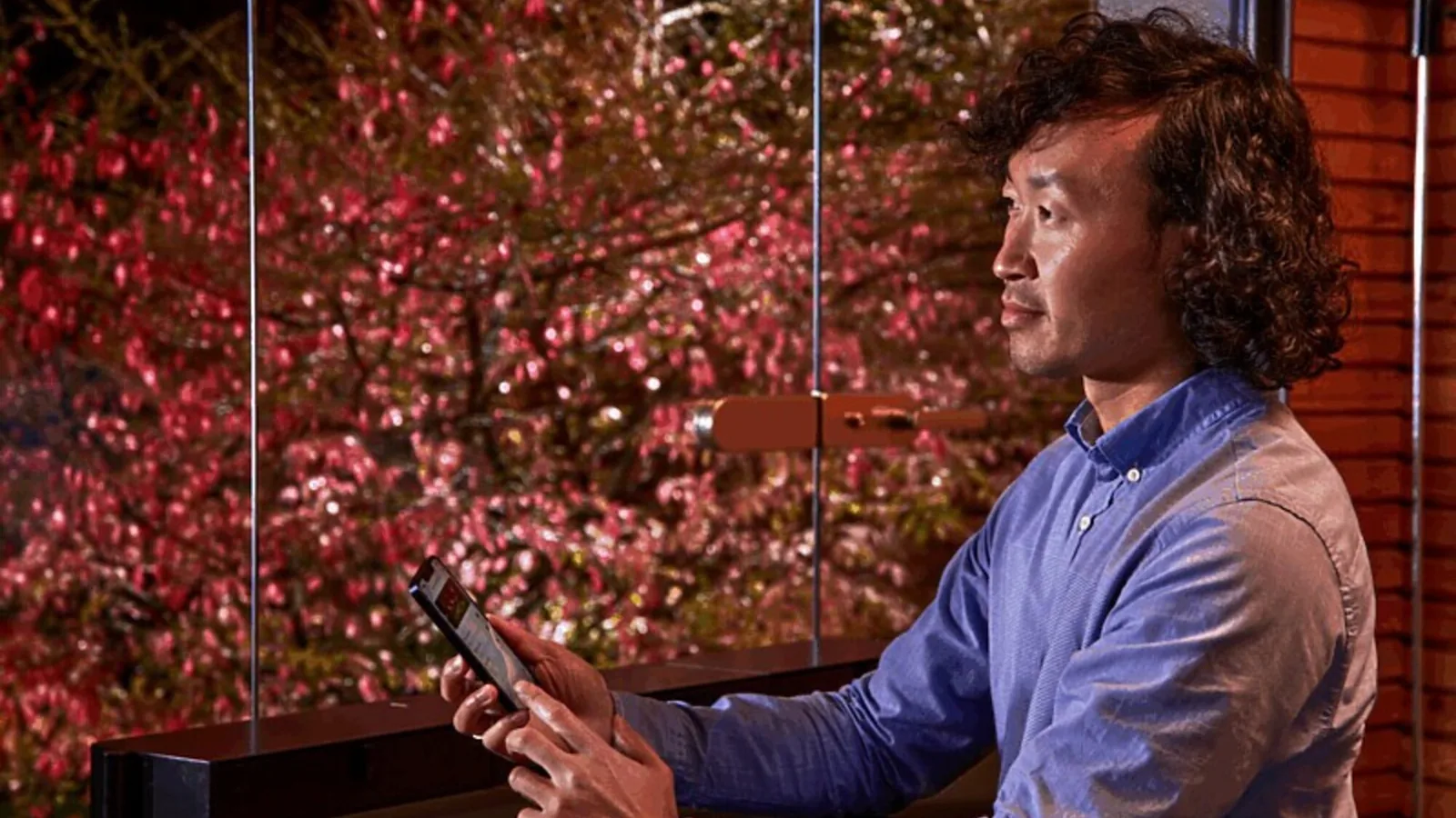 Mann på terrassen styrer hagelyset fra LunAqua Connect med OASE Switch-appen på mobilen om kvelden