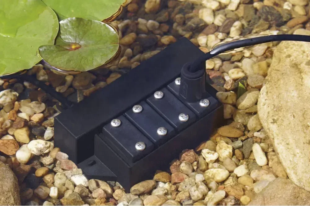 OASE LunAqua Power LED Driver i småstein ved vannkanten med spotkabler koblet til