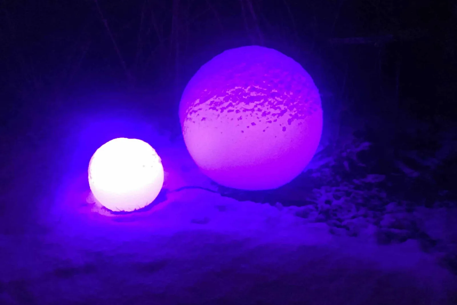 To lyskuler i plast lyser lilla med RGB-pære i snøen om kvelden
