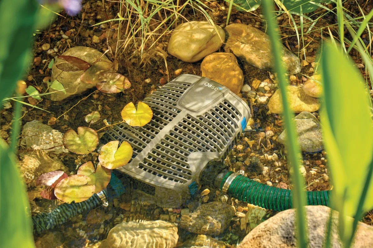 OASE AquaMax Eco Premium på bunnen av en hagedam mellom steiner og vannliljeblader, med slange tilkoblet
