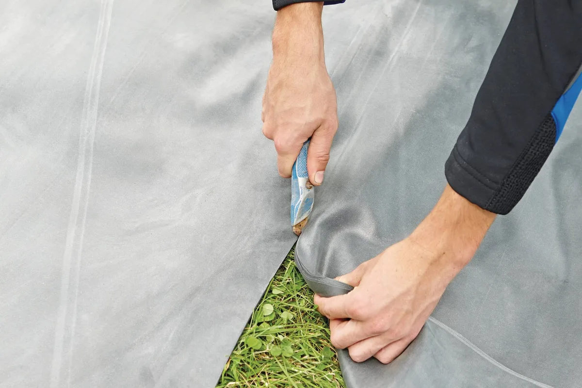 Svart EPDM-gummiduk fra OASE kuttes til med kniv på plenen