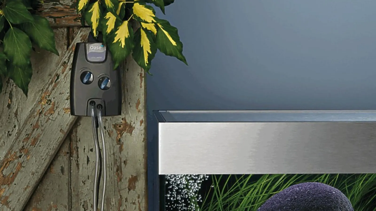 OASE OxyMax luftpumpe med to uttak henger på veggen ved et akvarium med bobler fra luftsteinen