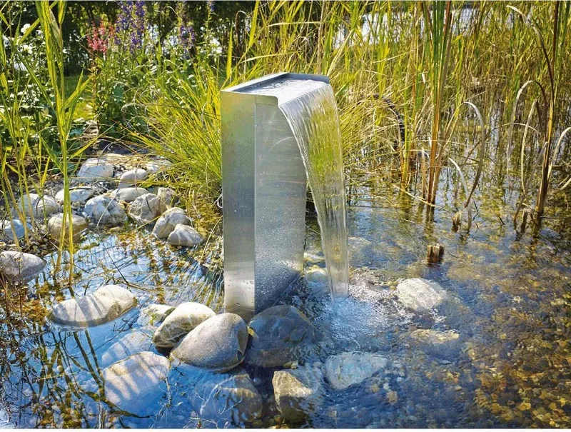 Vannfall med stålsøyle 30 cm i en dam med stein og siv